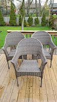 Three matching outdoor wicker-like chairs arranged on a wooden deck with some weathering visible.