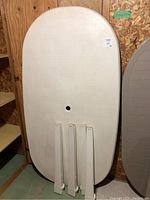 Photo showing the outdoor oval table top with four detachable legs laid against a wooden background. The table top is white with a center hole.