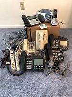 Wide shot of multiple office telephones including corded and cordless models, boombox radio/CD player, and cables.