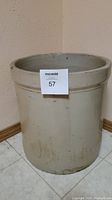 Full view of tall glazed clay pot with light beige color and dirt marks, standing on tiled floor.