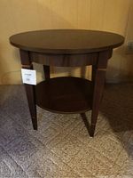 Side view of a round wooden side table showing the lower shelf and tapered legs