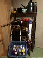 Photo of full shelf unit with items: blue basket filled with assorted light bulbs, metal step stool, extension cord, architectural balusters beside shelf.