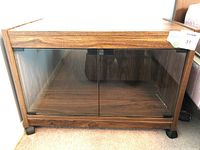 Front view of the TV stand showing two tinted glass doors, wood frame, and casters on the bottom.