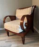 Photograph of a wooden arm chair with curved armrests, cane sides and backrest, and beige cushion with a circular pattern.