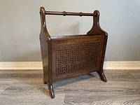 Full front-side view of the wooden magazine rack showing curved sides, cane panel front, and handle top