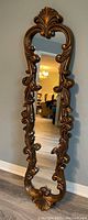 Full view of the tall ornate wall mirror showing carved scroll leaf frame and reflective glass.