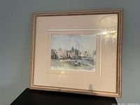 Full view of framed print artwork depicting a water landscape with buildings and boats, under a partly cloudy sky.