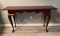Image showing the full sofa table placed against a wall, with a dark polished wood finish, carved curved legs ending in claw feet and a scalloped apron.