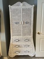 Front view of white wicker armoire with woven texture, two doors, and three drawers