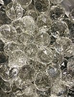 A pile of clear, round faceted chandelier crystals with varying reflections and light refractions visible.