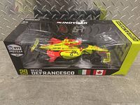 Front view of the boxed diecast 1:18 scale IndyCar model signed by Devlin DeFrancesco. Shows black and yellow packaging, clear plastic window to display car.