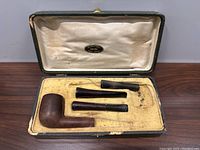 Open fitted case showing the wooden pipe bowl and three detachable stems arranged in custom slots within a velvet-lined yellow interior.