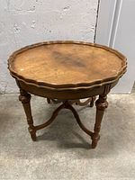 Front angled view of antique wooden side table showing scalloped tabletop edge, turned legs, and stretcher supports.
