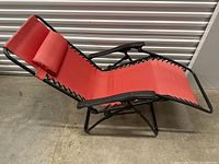 Side angle view showing the red fabric, black metal frame, adjustable back, and attached cushioning on the camping lounge chair.