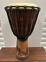 Front view of the hand carved djembe drum showing the tall wooden body, black rope tuning system, and natural skin head.
