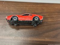Photo showing underside of red Hot Wheels Racebait 308 GTB diecast car with visible branding and model name on black base.