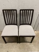 Front view of two IKEA dining chairs with dark wooden vertical slat backs and beige fabric seats.