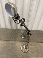 Full view of metal desk lamp showing adjustable arm with tension springs and clamp base on a metal surface.