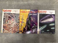 Three items spread side by side on a carpeted floor to show all covers. Left is Galaxy October 1953 with The Caves of Steel, center is Pebble in the Sky book, right is Galaxy October 1951.