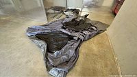 Large gray and black tent fabric laid out and somewhat folded on concrete floor.