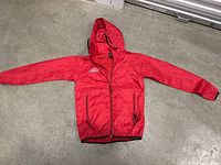 Full front view of red Nintendo windbreaker jacket with hood and zipper, laid flat on floor.