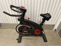 Side view of black and red SuperFit stationary exercise bike showing adjustable seat, resistance knob, and flywheel cover with brand name.