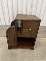 Front and side view showing overall form, top surface, side magazine holder with carved design, and closed storage cabinet with brass knob.