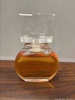 Front view of vintage Vanderbilt perfume bottle showing the amber liquid inside and clear sculpted cap with embossed design.