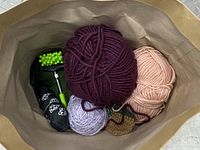 View of multiple yarn skeins and crafting accessories inside a brown bag