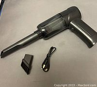 Black handheld 2-in-1 mini vacuum cleaner with slim nozzle attached, brush nozzle attachment, and USB charging cable on a table surface.