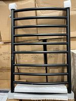 Luxury heated towel rail with multiple round horizontal bars, standing upright against a background of cardboard boxes with foam padding at top and bottom edges.