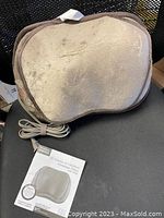 View of the closed plush massage pillow with power cord and instruction manual placed in front.