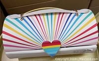 Front view of the rectangular jewelry box showing the rainbow-colored radiating stripe pattern and heart-shaped clasp on the faux leather exterior.