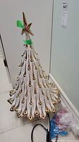 Full view of tall white ceramic Christmas tree with gold-tip branches and gold star on top, green tape visible on star.