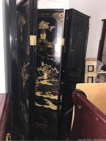 Full view of the six connected panels of the black lacquered Chinese room divider showing traditional hand-painted gold designs.