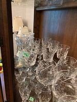 Several crystal glasses of varying heights and styles arranged on a mirrored shelf showing intricate cuts and stem designs.