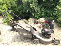 Left side view of Craftsman gas lawn mower with grass collection bag and surrounding garden pots.