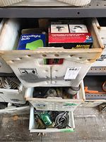 Three white plastic storage bins stacked on shelves filled with assorted lighting equipment and accessories.