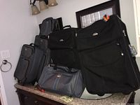 Front and side view of luggage set showing two large black Samsonite check-in suitcases and gray Cambridge Travelway carry-on bag.