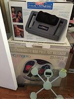 Boxes of Conair Shiatsu Massager and Chyer Electromagnetic Wave Pulse Foot Massager stacked with IKEA scale in front.