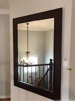 Mirror hung on wall, showing reflection of staircase and chandelier.