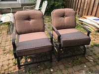 Two metal outdoor chairs with brown cushions positioned on patio floor.