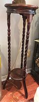 Full view of tall wooden plant stand showing three carved twisted legs and lower round shelf.