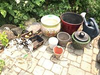 Photo showing all planters, plant stand, watering can and decorative box arranged outdoors on a paved surface with foliage in the background.