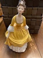 Front view of Royal Doulton Coralie figurine showing yellow dress, white polka dot sleeves and underskirt, facial details, and glossy finish.