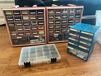 Four organizers placed on floor containing various sewing supplies like thread spools and buttons.