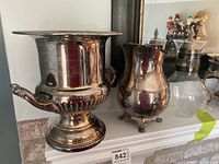 Lot showing silver plate ice bucket, silver plate pitcher with missing handle, and glass carafe with silver-tone neck and stopper arranged on white shelf.