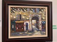 Framed painting showing the street scene with shop fronts and archway, signed by W. James.