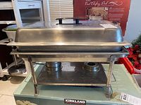 Front view of the larger warming tray with lid and legs, showing the bulk and elevation.