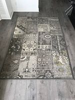 Full view of light beige patchwork area rug laid on gray hardwood floor, showing overall pattern and condition.